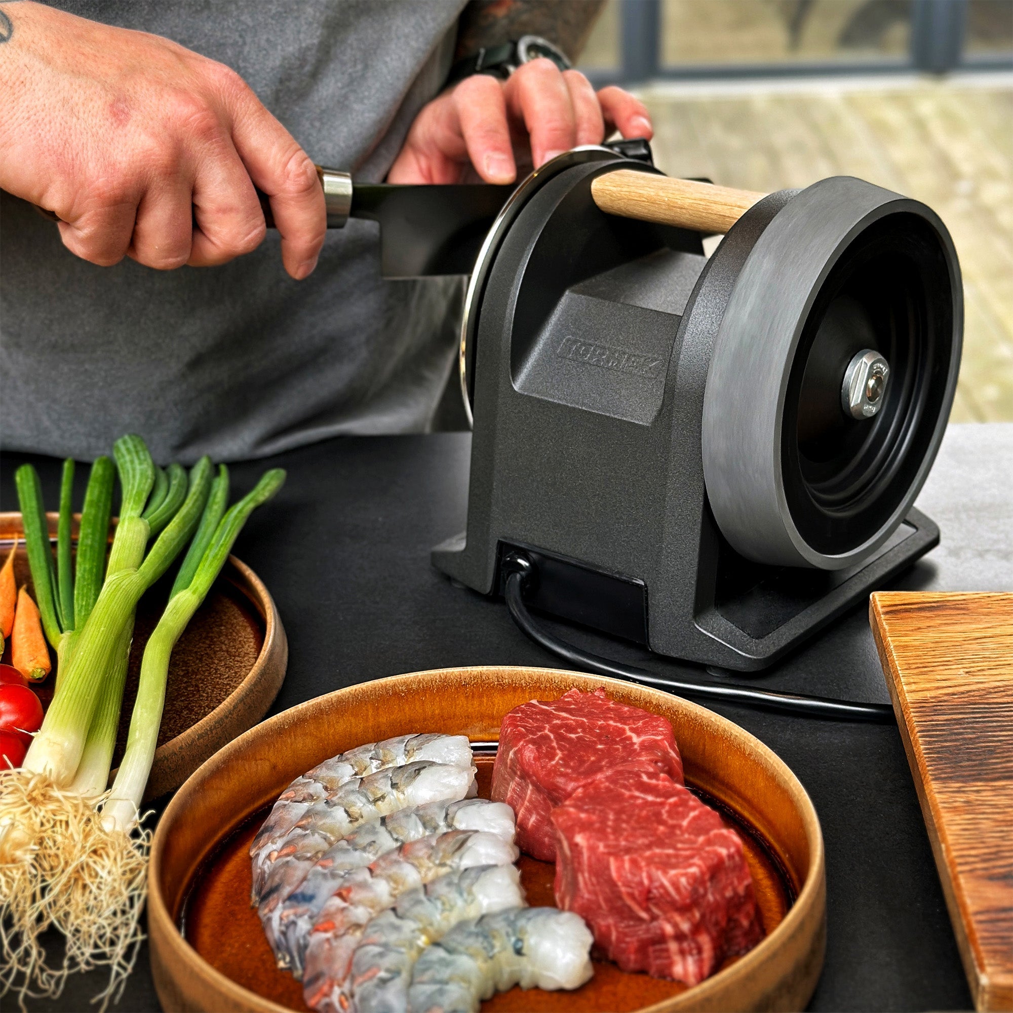 A person sharpening a knife on the Tormek T-1 Carbon Black in a kitchen setting among ingrediens